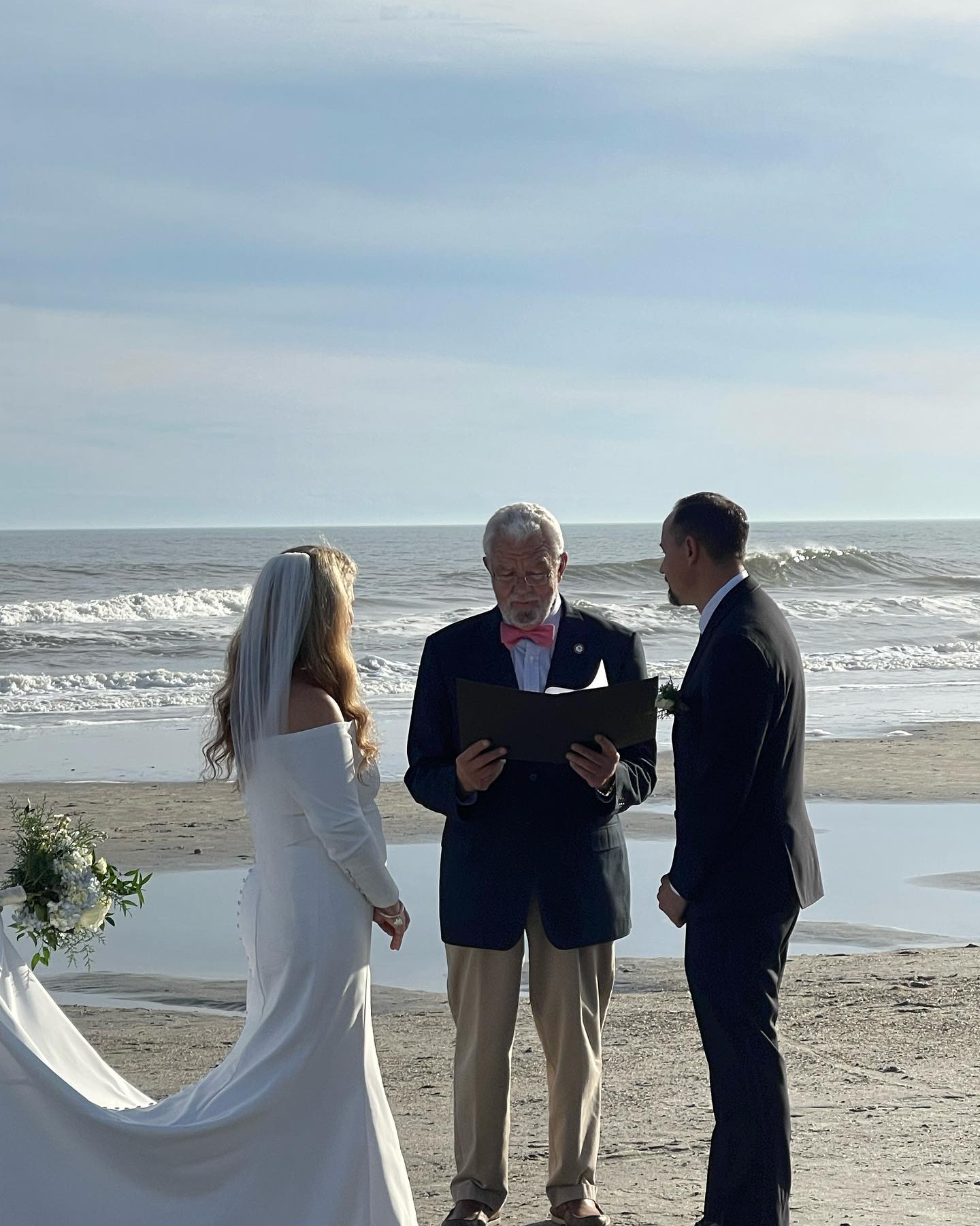 A beach wedding ceremony with a couple and an officiant on the shore.